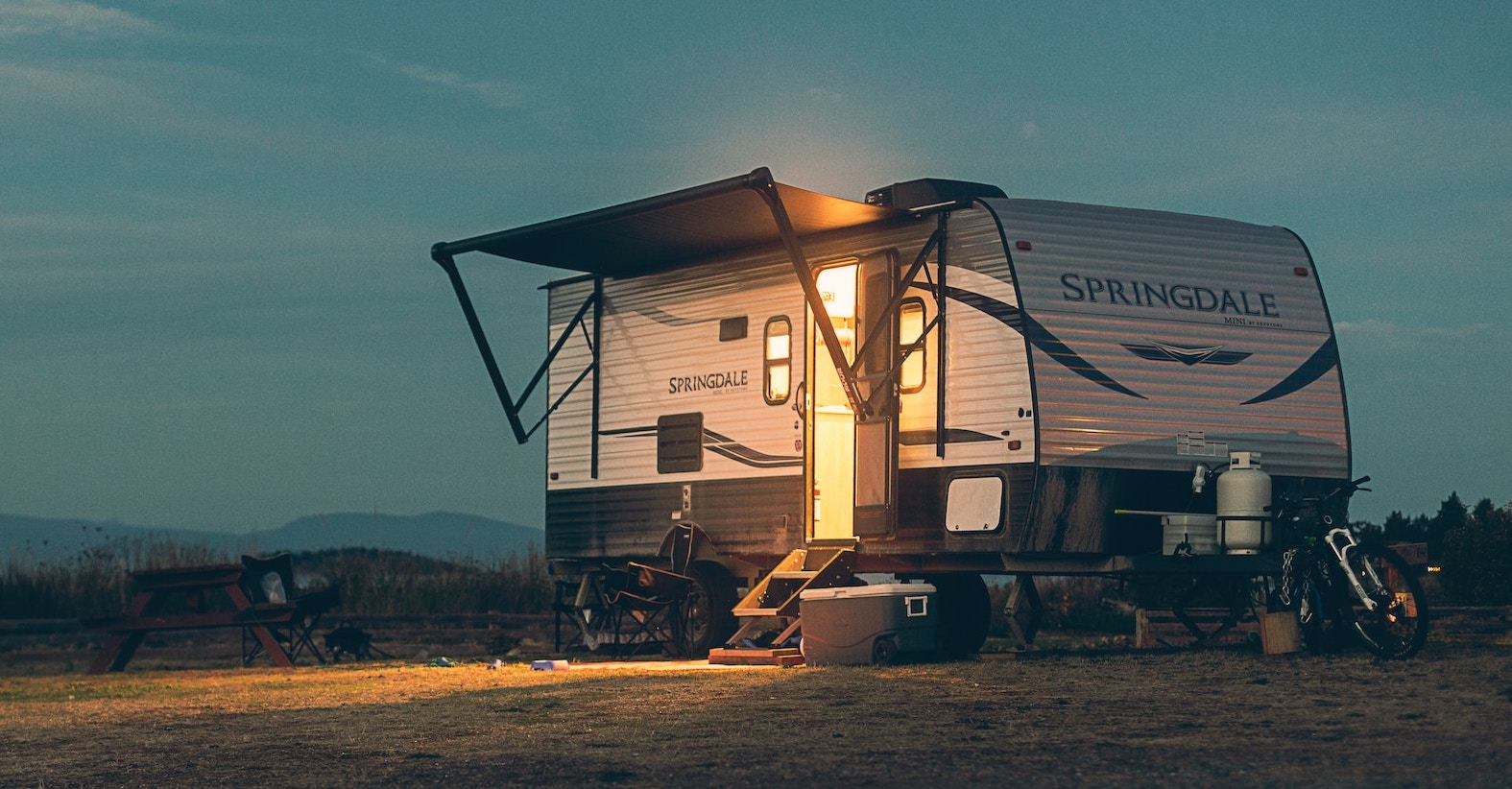 Camper with a light on parked in an open field under a night sky